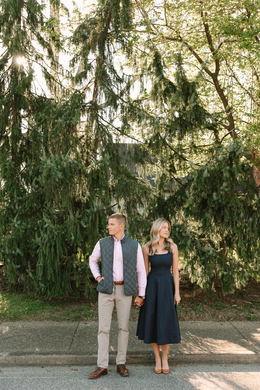 Katherine and Jackson embracing during their Evansville Indiana engagement session with golden sunlight and evergreen trees.