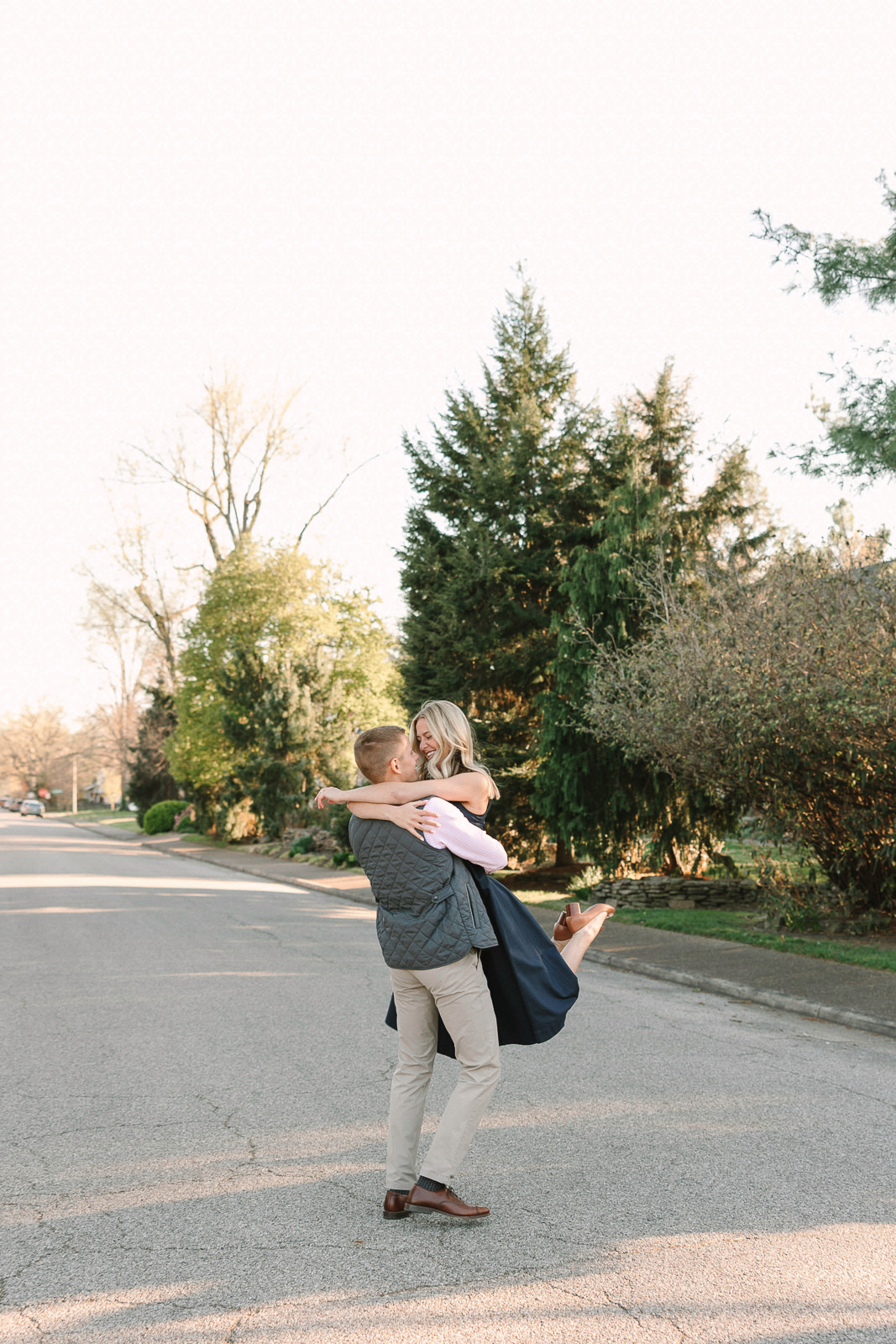 Katherine and Jackson embracing during their Evansville Indiana engagement session with golden sunlight and evergreen trees.