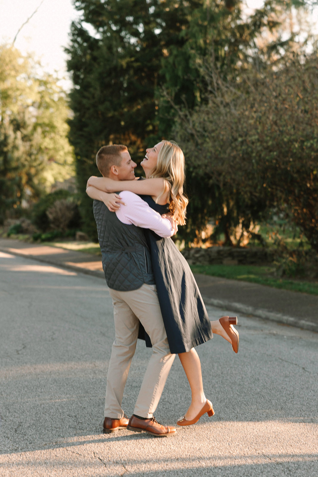 Katherine and Jackson embracing during their Evansville Indiana engagement session with golden sunlight and evergreen trees.