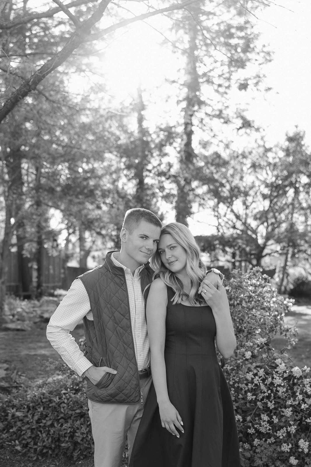 Katherine and Jackson embracing during their Evansville Indiana engagement session with golden sunlight and evergreen trees.