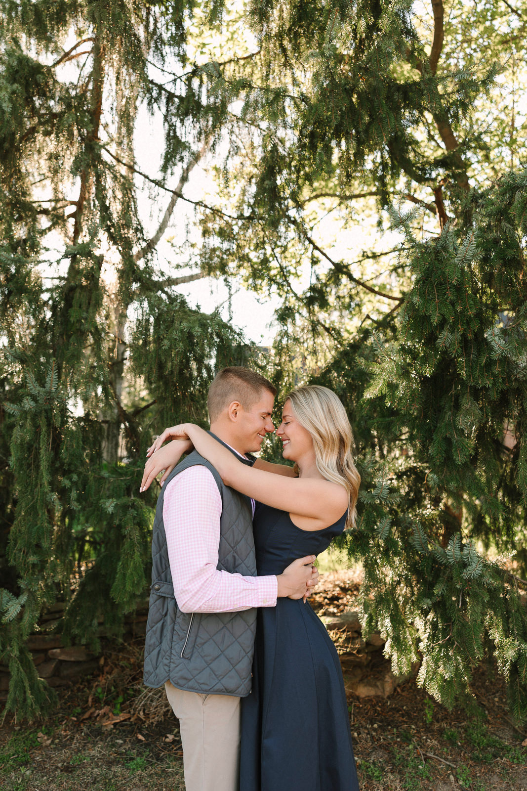 Katherine and Jackson embracing during their Evansville Indiana engagement session with golden sunlight and evergreen trees.